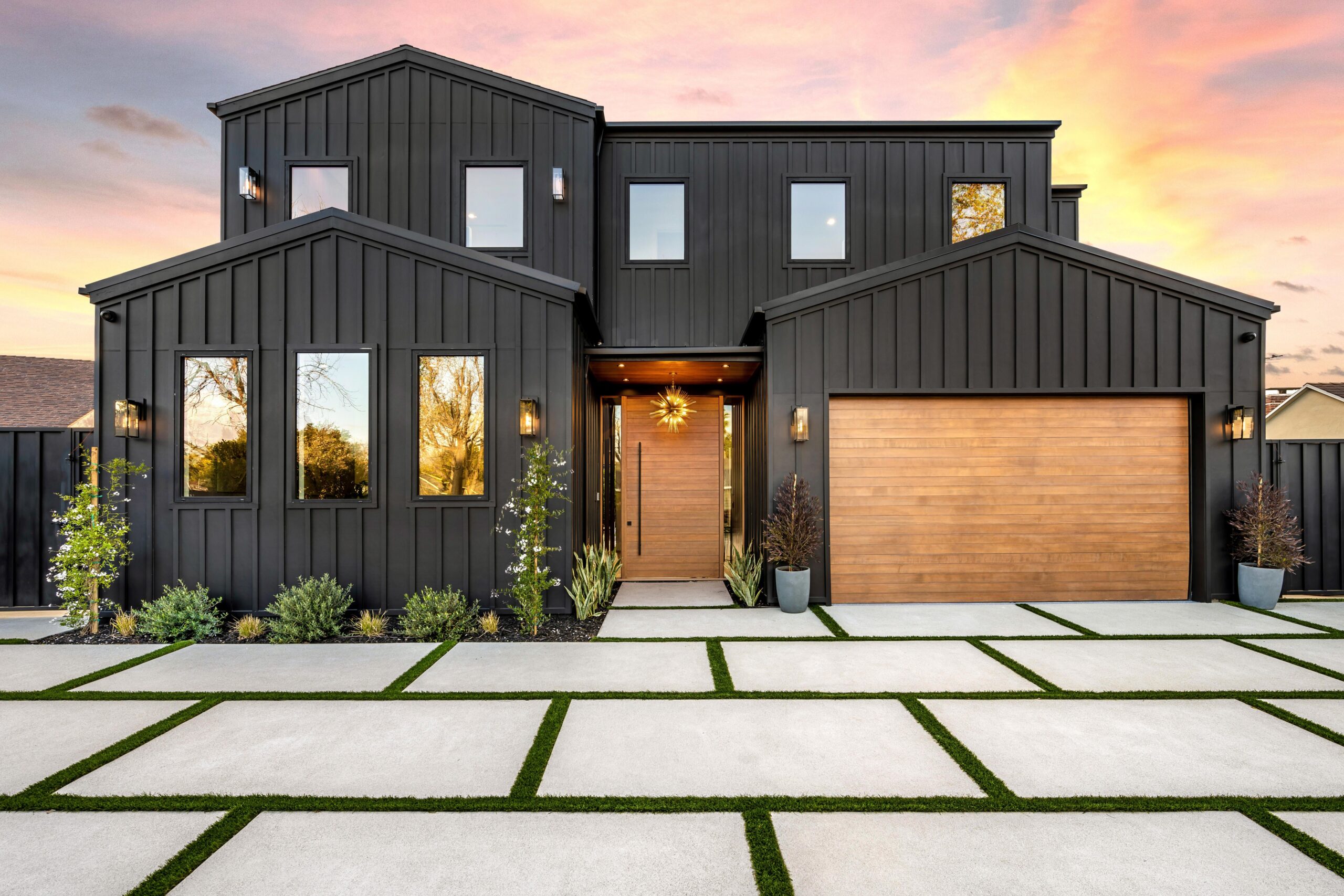 Contemporary black house exterior with wooden garage door. Modern black house exterior with wooden garage door and driveway at sunset.