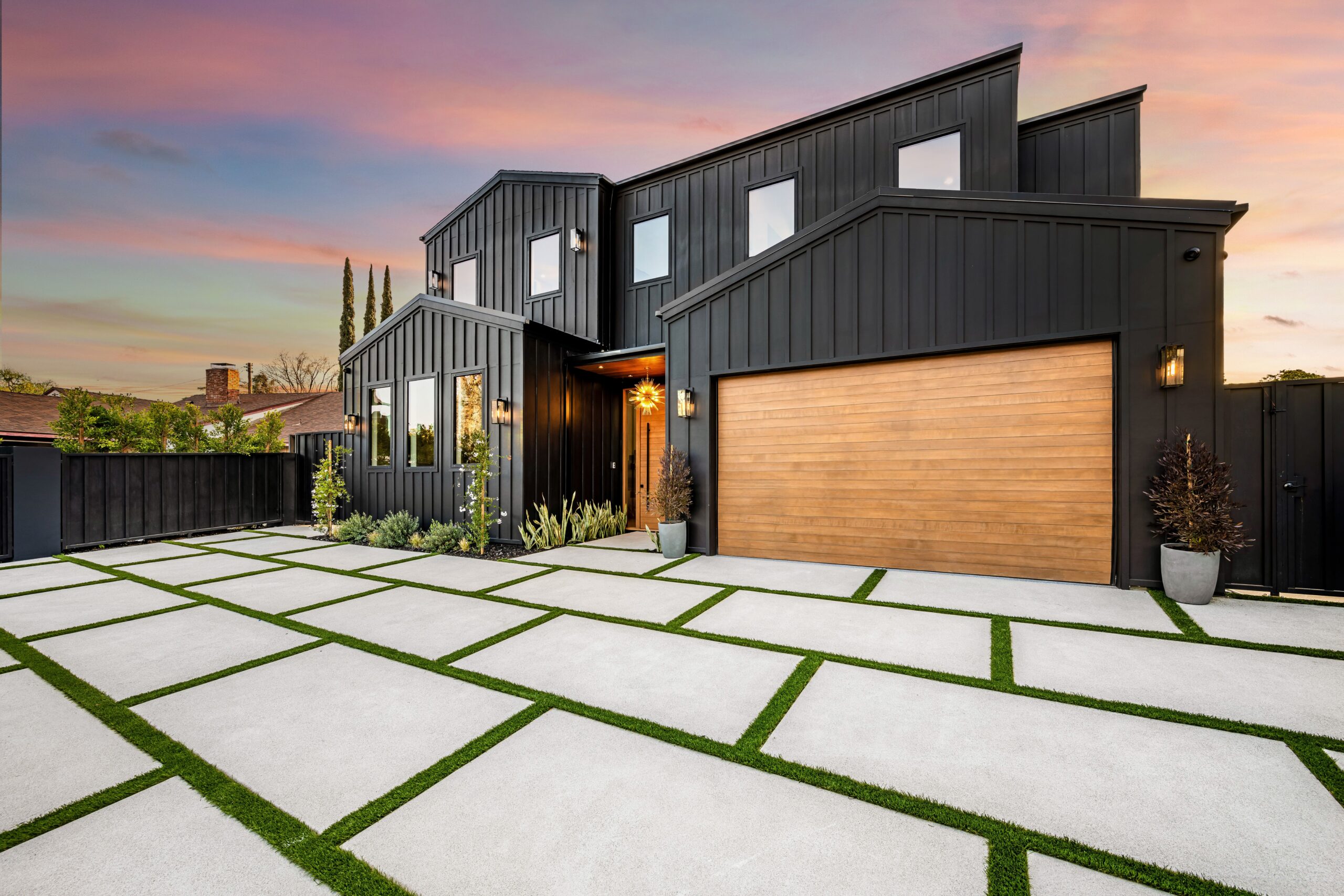 Modern black house with wooden garage door and geometric driveway. Modern black house exterior with a wooden garage door and a geometric driveway at sunset.